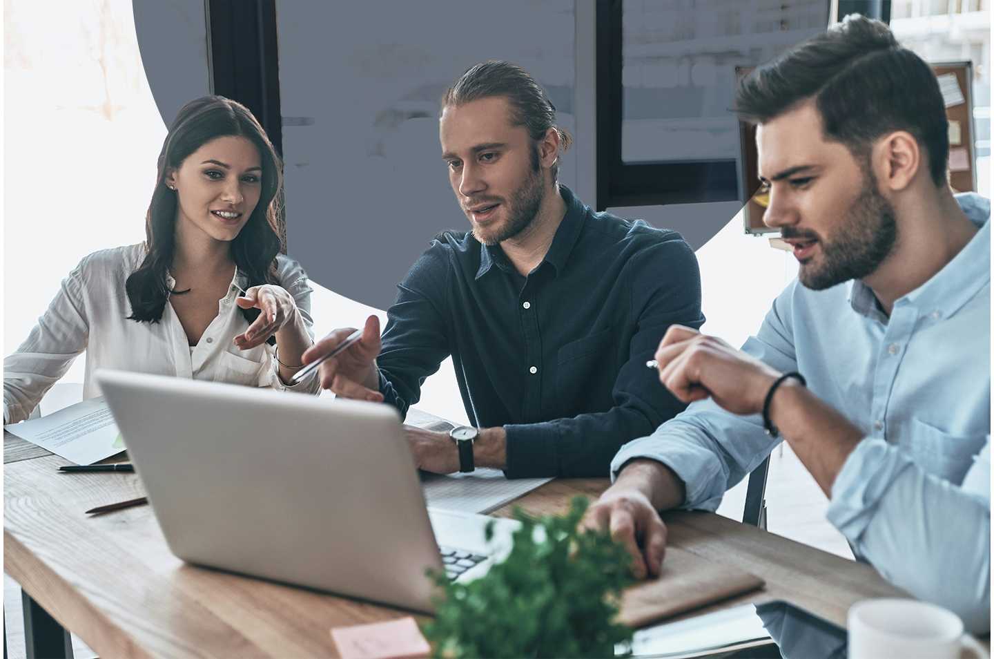 two men and a woman sitting around a computer at a desk