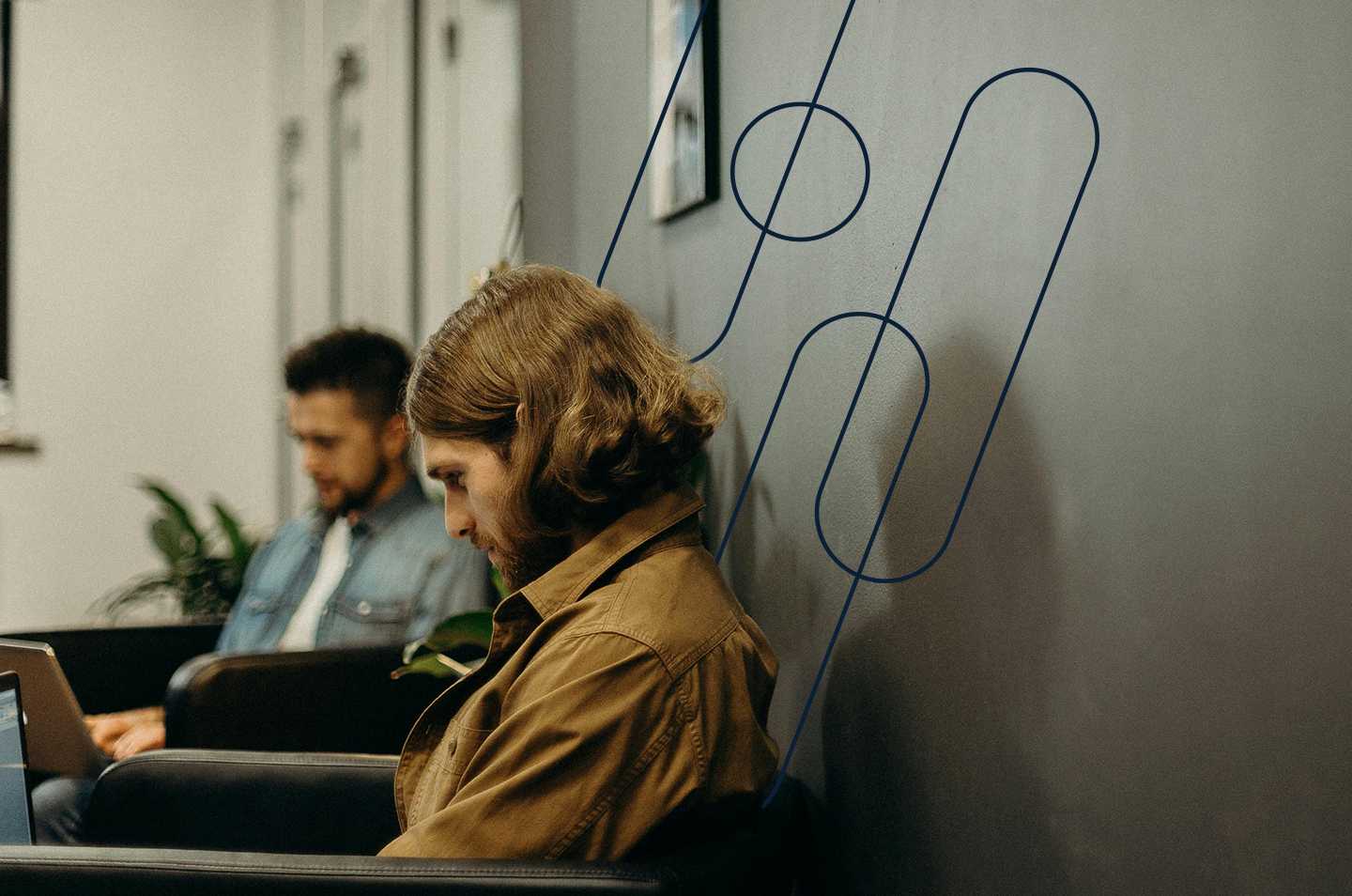 a man sitting against a wall looking down at a laptop