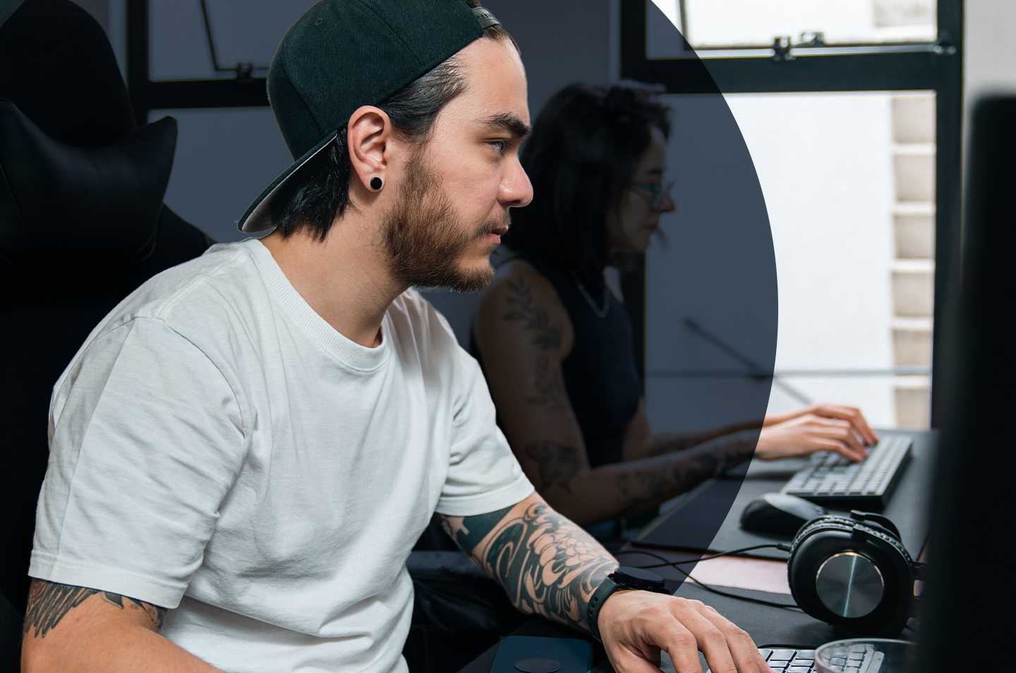 a man sitting at a desk wearing a backwards hat